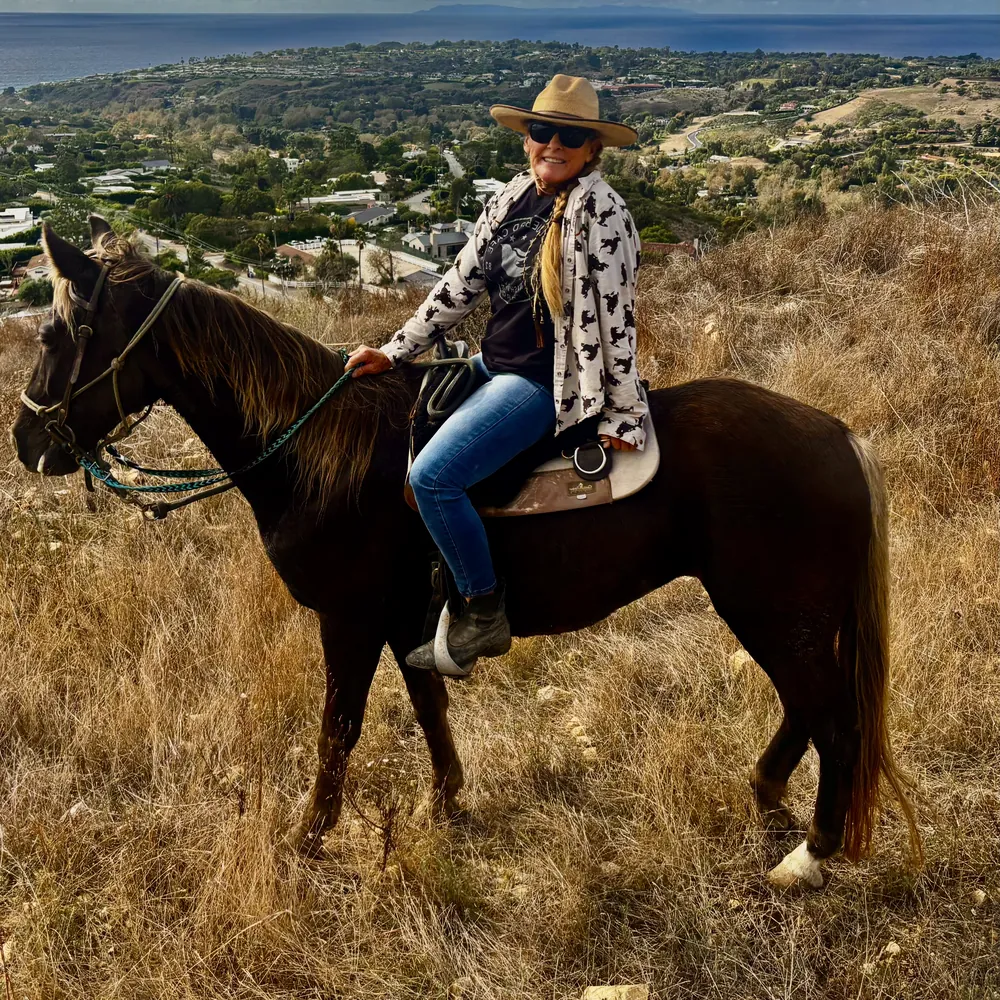 A rider in a straw hat on Starlight, a dark brown horse with a flaxen mane, above the coast