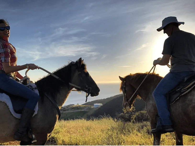 Two riders silhouetted at sunset above the ocean