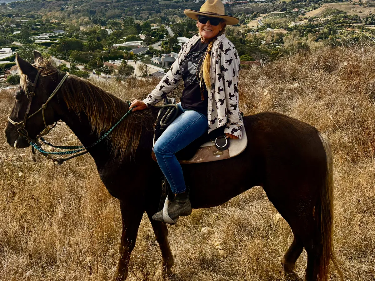 A rider in a straw hat on Starlight, a silver dapple mare, above the coast