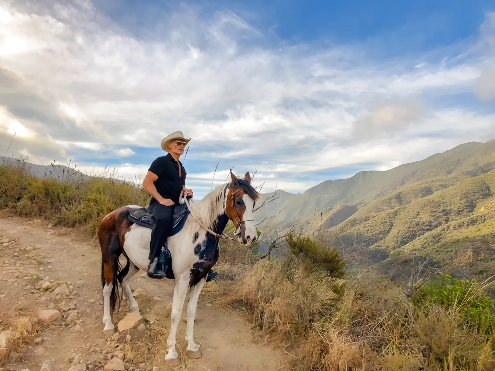 A rider in a hat on a paint horse on the trail under big clouds